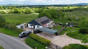 Aerial view of a rural house with scaffolding, two black vans, fields and trees